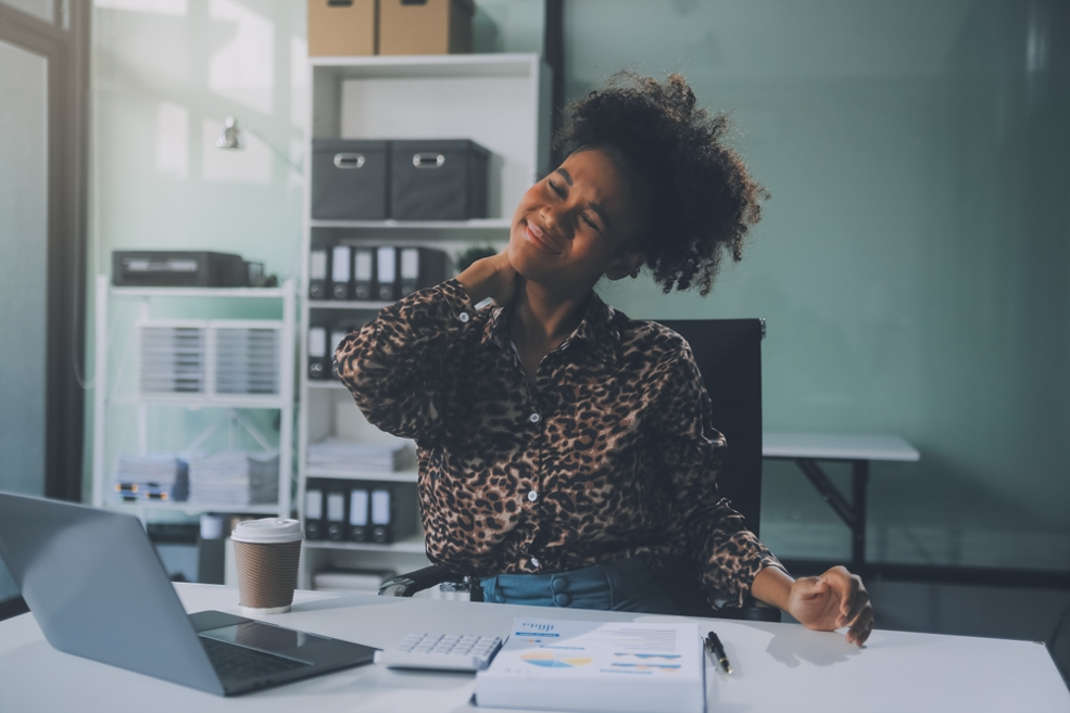 Woman at desk with tech neck wincing and holding neck in pain